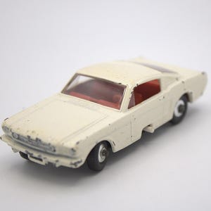 May include: White toy car model of a Ford Mustang. The car has a red interior and black wheels.