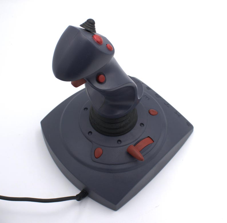 Puede incluir: Un joystick gris oscuro con botones y detalles en rojo. El joystick tiene una parte superior redondeada y una base con botones adicionales y una palanca de control. Un cable negro se extiende desde la base.