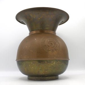 May include: A vintage brass tobacco humidor with a wide opening and a round body. The humidor has a brass band around the middle with the text "Mail Order 5 Cents Cigars" embossed on it.