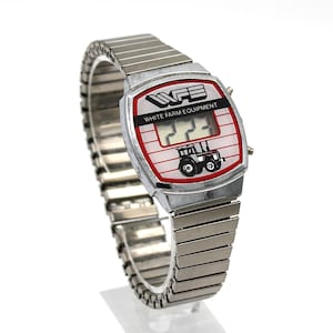 Peut inclure: Une montre-bracelet argent&eacute;e vintage avec un cadran rectangulaire. Le cadran affiche le texte "WFE WHITE FARM EQUIPMENT" et un dessin de tracteur. La montre a un bracelet extensible argent&eacute;.