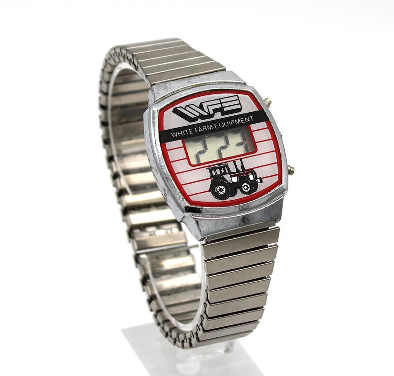 Peut inclure: Une montre-bracelet argent&eacute;e vintage avec un cadran rectangulaire. Le cadran affiche le texte "WFE WHITE FARM EQUIPMENT" et un dessin de tracteur. La montre a un bracelet extensible argent&eacute;.