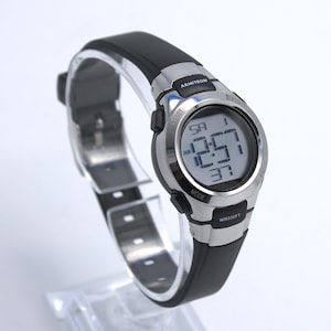 May include: A digital Armitron watch with a black rubber strap and a silver-tone bezel. The watch face displays the time and date. The watch is water resistant to 330 feet.
