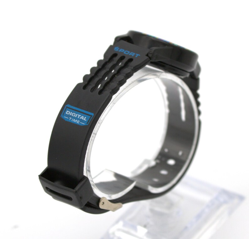 May include: Black digital sport watch with a blue accent on the face and band. The watch band has the words "DIGITAL - TIME-" in a blue rectangle. The word "SPORT" is printed in blue on the watch face.