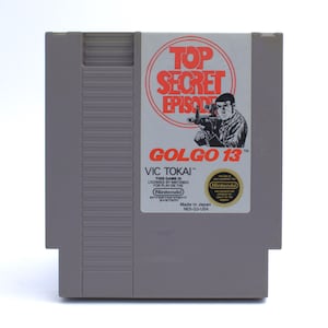 May include: A gray Nintendo NES game cartridge for "Golgo 13: Top Secret Episode." The label features a man holding a gun, the game title, and the Nintendo logo. The cartridge is labeled "Made in Japan."