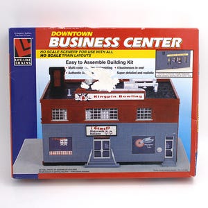 May include: A model kit box for a Downtown Business Center, featuring a multi-colored building with the text "Kingpin Bowling" and "i Gemelli Ristorante Italiano". The box includes the Life-Like Trains logo and states it is for HO scale train layouts.