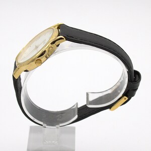 May include: A gold-toned wristwatch with a white face and black leather band. The watch has a classic design with a round face and a buckle closure. The watch is displayed on a clear stand against a white background.