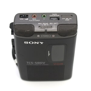 May include: A black Sony TCS-580V stereo cassette recorder with a built-in microphone and speaker grilles. The device has a tape counter, volume control, and various input/output jacks. The model name and brand are visible on the front.