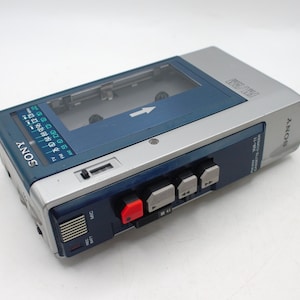 May include: A vintage Sony WM-11 cassette player in silver and blue. The portable audio device features a cassette compartment, control buttons, and a radio dial. The Sony logo is visible on the front and side of the player.