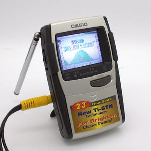 May include: A silver and black Casio handheld television with a 2.3 inch screen displaying the Super Mario World title. The device features a retractable metal antenna, a yellow input cable, and a sticker promoting New Ti-STN Technology.