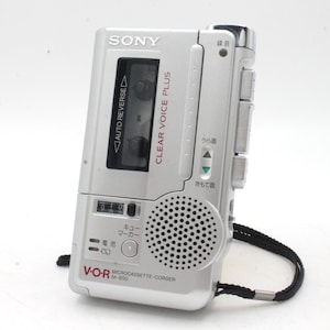 May include: A silver Sony V-O-R microcassette recorder with a black strap. The recorder has a clear voice plus feature and a counter display. The text on the recorder reads "CLEAR VOICE PLUS" and "MICROCASSETTE-CORDER M-850".