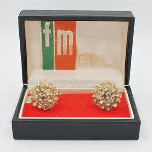 May include: A black box with a red and green label that says "fm for the man". Inside the box are two gold cufflinks.