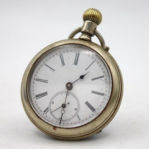 May include: Antique pocket watch with a white face, black Roman numerals, and a smaller seconds dial. The watch has a silver-colored case and a gold-colored crown. The glass has some cracks. A classic timepiece.