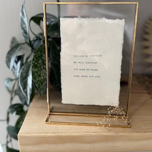 Pu&ograve; includere: Una stampa incorniciata con il testo "You are my sunshine, my only sunshine, you make me happy, when skies are grey." La cornice &egrave; dorata e rettangolare, con un fronte in vetro trasparente. La carta all'interno &egrave; bianco sporco.