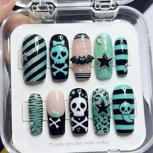 May include: A set of press-on nails with various designs. The nails feature black and teal stripes, skulls, bats, stars, and leopard print patterns. Some nails have a matte finish, while others have a glossy finish. The text "Thank you for your order" is visible.