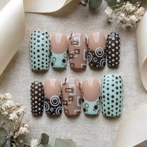 May include: A set of ten press-on nails featuring a variety of designs including light mint green with brown polka dots, nude with brown and white geometric squares, nude with brown swirls, and dark brown with light mint green polka dots.