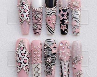 May include: A set of ten long, artificial nails with various designs. The nails feature pink, white, and black bases, adorned with glitter, rhinestones, animal prints, and star accents. Some nails have zebra stripes, while others showcase heart and lace patterns.