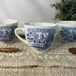 Peut inclure: Trois tasses à thé blanches avec des motifs de paysages bleus. Chaque tasse a une anse et une soucoupe assortie. Les tasses sont posées sur une surface texturée de couleur crème, avec des cuillères en bois à proximité. Les tasses à thé sont de conception classique.