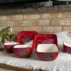 Peut inclure: Un ensemble de plats de service en céramique rouge avec un motif de raisin. L'ensemble comprend des assiettes carrées et des bols avec un intérieur blanc. Le motif de raisin présente des raisins violets et des feuilles vertes.