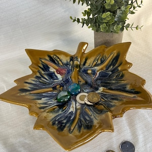 Peut inclure: Un plat en céramique en forme de feuille avec un extérieur marron brillant et un design intérieur bleu et blanc. Le plat contient de petites pierres colorées et des pièces de monnaie. Une petite plante en pot est en arrière-plan.