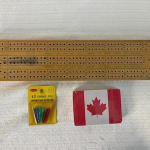 Peut inclure: Un plateau de cribbage rectangulaire en bois avec des pistes numérotées, un emballage blister jaune contenant douze pions de cribbage en plastique bleu, vert et rouge, et un jeu de cartes avec un motif de feuille d'érable canadienne rouge et blanc.