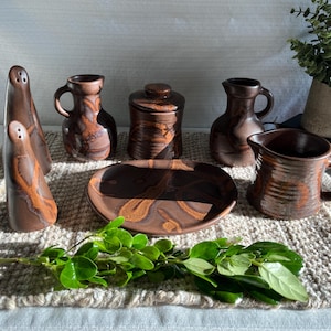 Peut inclure: Ensemble de céramiques marron comprenant salières et poivrières, petits pichets, un pot avec couvercle, une assiette et un pichet avec anse. Les pièces présentent un motif marbré et sont disposées sur un tapis beige texturé.