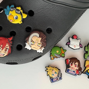 May include: A black clog shoe decorated with various colorful rubber character charms. The charms feature stylized anime-inspired figures including a yellow bird, a red-haired character, a dark-haired character, a green creature, a white creature, a cactus, a blonde character, a brown-haired character, and a wizard-like figure.