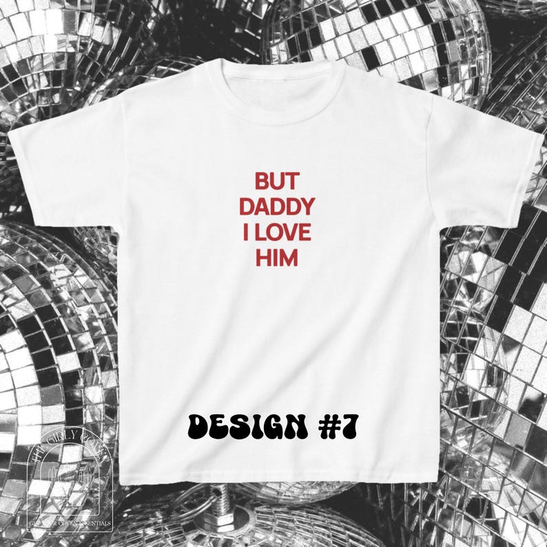 Puede incluir: Una camiseta blanca de manga corta con el texto rojo BUT DADDY I LOVE HIM centrado en el pecho. Debajo del texto, las palabras DESIGN #7 est&aacute;n impresas en una fuente negra, negrita y ondulada. La camiseta tiene cuello redondo y corte est&aacute;ndar.
