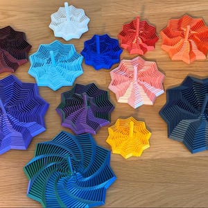May include: A collection of colorful, layered, star-shaped objects with a central stem. The objects are in various colors, including white, blue, red, orange, pink, purple, green, and yellow. They are arranged on a wooden surface.