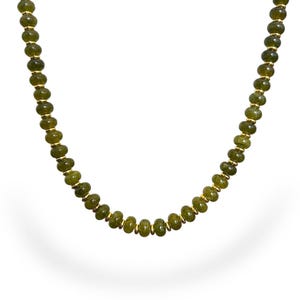 Puede incluir: Un collar que presenta una hilera continua de pequeñas cuentas redondas de color verde oliva intercaladas con diminutos espaciadores de metal en tono dorado pulido. Las cuentas tienen un aspecto liso y semitranslúcido en un patrón uniforme.