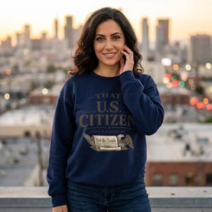 May include: A navy blue sweatshirt with the text "THAT U.S. CITIZEN" in gold lettering. Below the text is an illustration of an eagle and a scroll that reads "We the People". The sweatshirt is worn by a person.