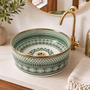 May include: A round ceramic basin with a green and white pattern and a gold rim. The basin is set on a light-coloured surface, with a gold tap and a decorative mirror in the background. The sink's diameter is approximately 40 cm.