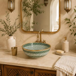 May include: A bathroom vanity with a decorative sink. The sink is white with a green and gold pattern. A gold-framed mirror hangs above the sink. Decorative wall sconces and a wooden cabinet complete the scene.