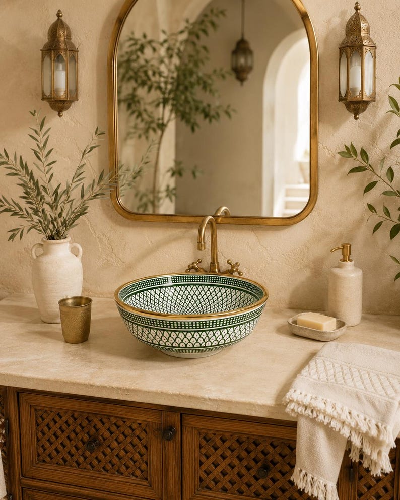 May include: A bathroom vanity with a decorative sink. The sink is white with a green and gold pattern. A gold-framed mirror hangs above the sink. Decorative wall sconces and a wooden cabinet complete the scene.