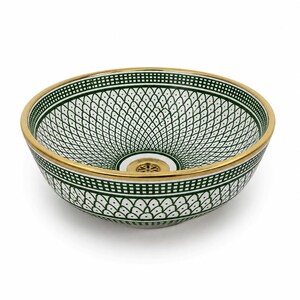 May include: A decorative ceramic sink basin with a white and green geometric pattern. The rim and drain are gold-colored. The sink has a round shape and is designed for bathroom use.
