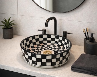 May include: A round ceramic vessel sink featuring a black and white checkered pattern with a gold-toned drain. The sink is equipped with a matte black faucet and two matching handles, set against a light gray tiled wall and countertop.