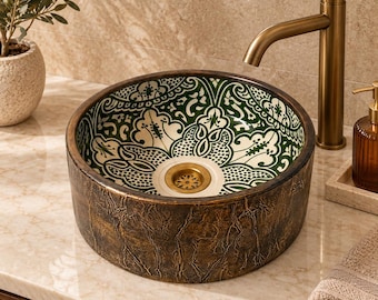 May include: A round vessel sink featuring a textured, dark bronze-colored exterior and an interior decorated with a green and white floral pattern. The sink includes a brass-toned drain and is paired with a tall, matching brass-toned faucet.