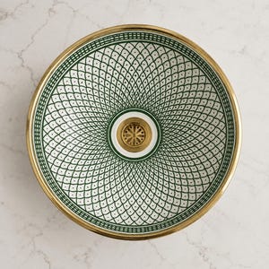 May include: A decorative sink basin with a gold rim and a white and green patterned interior. The basin features a central drain with a gold finish. The intricate design is a repeating pattern of green diamonds and dots.