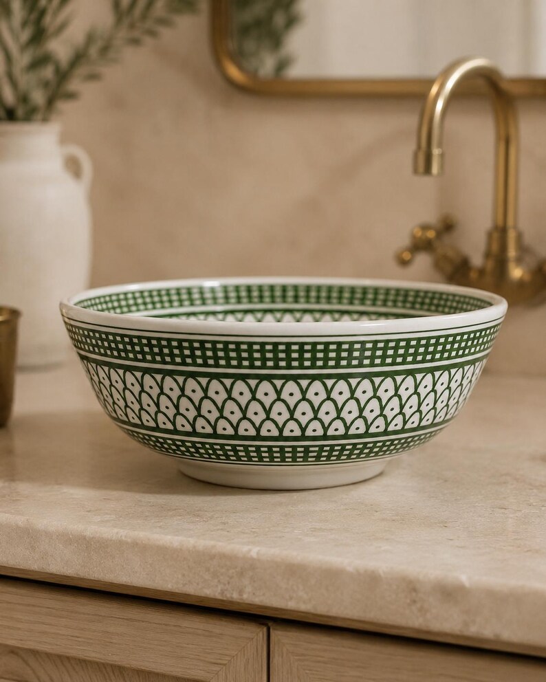 May include: A white ceramic bowl with a green geometric pattern. The bowl features a repeating design of small, connected teardrop shapes and a border of green squares. The bowl is sitting on a light-colored countertop.