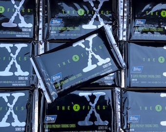 May include: A stack of nine trading card packs featuring the X-Files logo. Each pack is black with a silver foil design and the text "The X-Files" and "Series One". The packs are from Topps and contain 9 super premium trading cards.