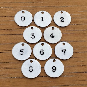 May include: Ten silver metal round tags with numbers 0 through 9 printed on them.