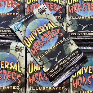 May include: A close-up of a stack of trading card packs featuring Universal Monsters. The packs are silver with a black background and feature a globe with a chain and a Universal Monsters logo. The text on the packs reads "Universal Monsters Illustrated" and "8 Deluxe Trading Cards".