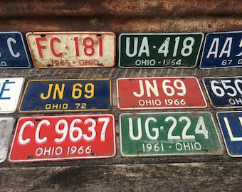 May include: A collection of vintage Ohio license plates with various colors and numbers. The plates are made of metal and have a distressed look. The plates include the following numbers: FC-181, UA-418, AA 5, JN 69, 650, CC 9637, UG-224, and LI.