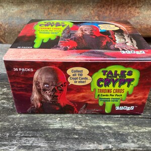 Puede incluir: Una caja de cartas coleccionables de Tales from the Crypt. La caja es roja y verde con una sustancia verde viscosa que gotea por la parte delantera. La caja presenta un monstruo con la cara verde y una mujer con el pelo largo y rubio. El texto de la caja dice "Tales from the Crypt Trading Cards 8 Cards Per Pack Randomly Packed Promo Cards".
