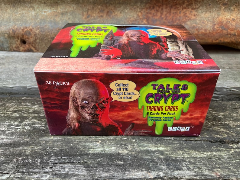 Puede incluir: Una caja de cartas coleccionables de Tales from the Crypt. La caja es roja y verde con una sustancia verde viscosa que gotea por la parte delantera. La caja presenta un monstruo con la cara verde y una mujer con el pelo largo y rubio. El texto de la caja dice "Tales from the Crypt Trading Cards 8 Cards Per Pack Randomly Packed Promo Cards".
