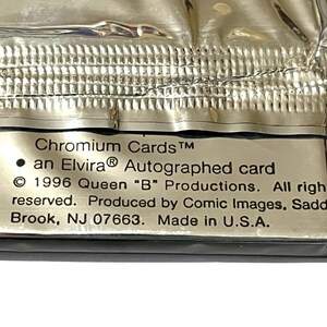 Puede incluir: Primer plano de un paquete sellado de "Chromium Cards" con una tarjeta autografiada de Elvira. El embalaje plateado y met&aacute;lico tiene texto que indica la producci&oacute;n de la tarjeta por Comic Images en 1996, fabricado en EE. UU.