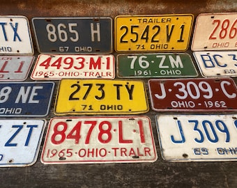 May include: A collection of vintage Ohio license plates in various colors and designs. The plates feature different numbers, letters, and dates, including "865 H", "2542 V1", "286", "4493-M-1", "76-ZM", "BC 30", "78 NE", "273 TY", "J-309-C", "3ZT", "8478-L-1", and "J 3090".