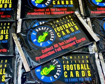 May include: A close-up of a stack of sealed packs of Classic Draft Picks Limited Edition Football Cards. The packs are black with a blue and yellow circle logo that says "Classic Draft Picks". The text on the packs reads "Limited Edition Football Cards", "10 Cards Per Pack", "Collect All Ten Limited Production Foil Stamped Cards".