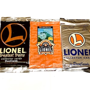 May include: Three unopened packs of Lionel collector cards. The packs are in black, orange, and silver packaging. The Lionel logo, a stylized "L" inside a circle, is prominently displayed on each pack. Text includes "Greatest Trains" and "Collector Cards".