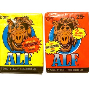 May include: Two vintage trading cards featuring Alf, an alien character from the 1980s television series. The cards are yellow and orange with blue circles and text that reads "Special Bouillabaseball Card Inside!" and "New Bouillabaseball Card Inside!" The cards also feature the text "ALF" and "2nd Series".