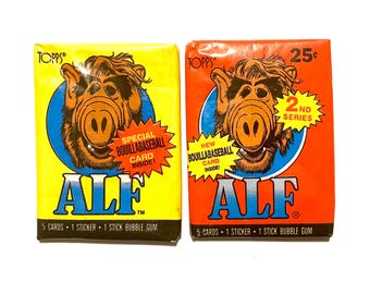 May include: Two vintage trading cards featuring Alf, an alien character from the 1980s television series. The cards are yellow and orange with blue circles and text that reads "Special Bouillabaseball Card Inside!" and "New Bouillabaseball Card Inside!" The cards also feature the text "ALF" and "2nd Series".
